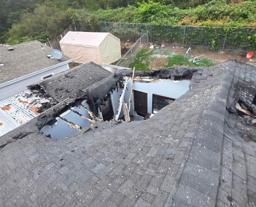 High-angle view of a catastrophic residential roof collapse caused by fire or storm damage, illustrating the need for rapid structural stabilization and tarping services in the Seattle area.