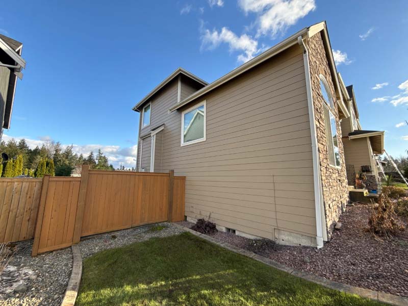 Side profile of a multi-story home featuring a combination of tan lap siding, stone masonry, and professional fascia trim work.