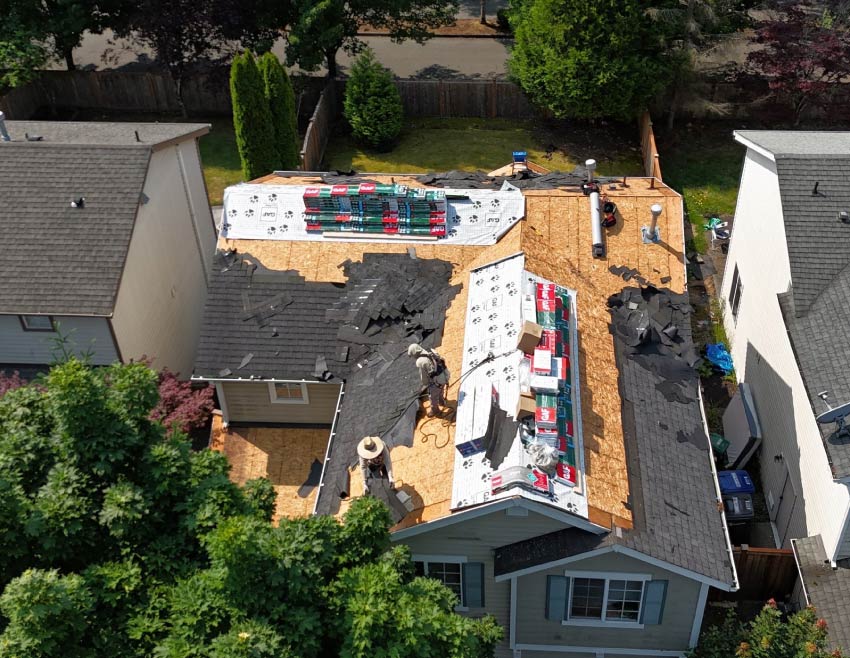 GAF Certified roofing crew performing a full roof replacement; visible structural decking and stacks of GAF Timberline HDZ shingles ready for installation.