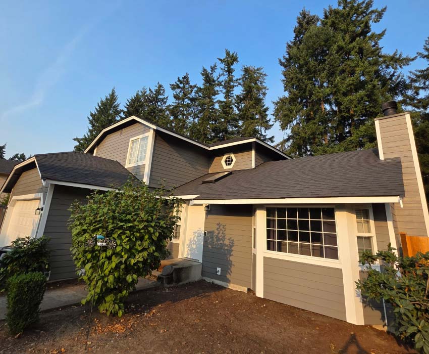 Front exterior view of a multi-level suburban home featuring a fresh gray paint job with contrasting white trim, a dark asphalt shingle roof, and tall pine trees in the background.