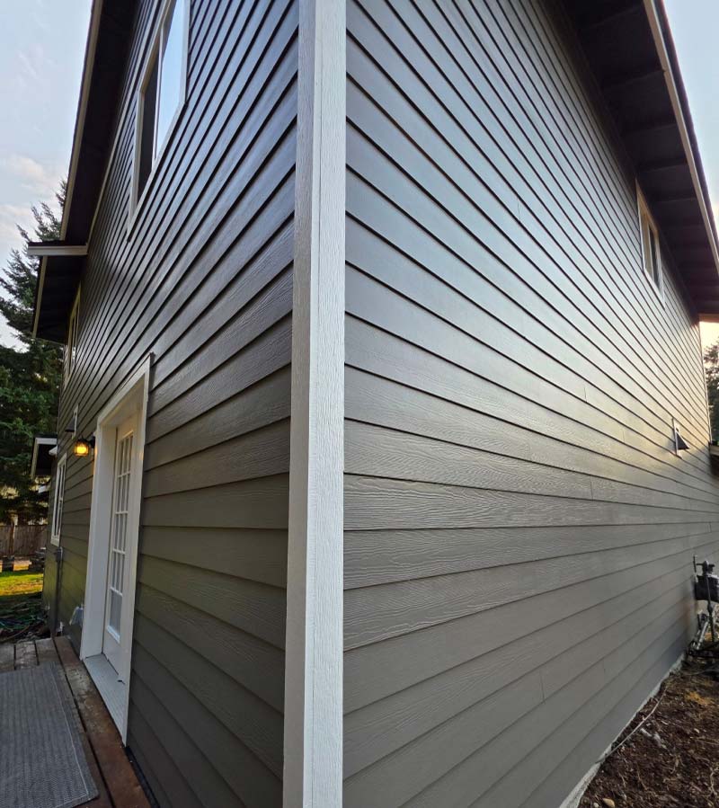 Close-up exterior view of a home's corner showcasing newly painted gray horizontal lap siding accented by clean white vertical trim and a white door frame.