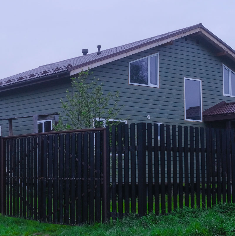 Modern black vertical privacy fence installed alongside green horizontal siding, custom fence installation Seattle WA