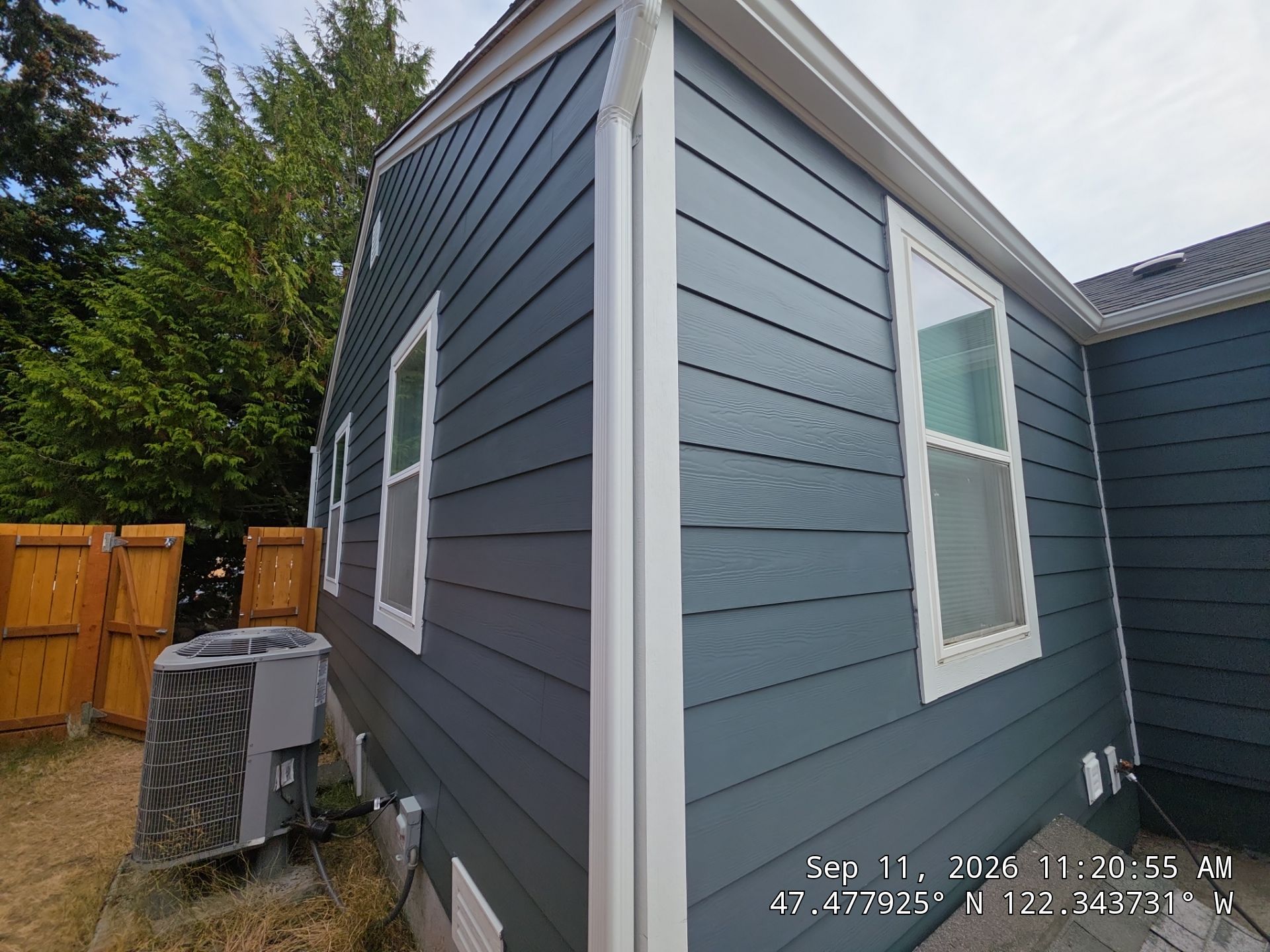 Side profile of a multi-story home featuring a combination of tan lap siding, stone masonry, and professional fascia trim work.